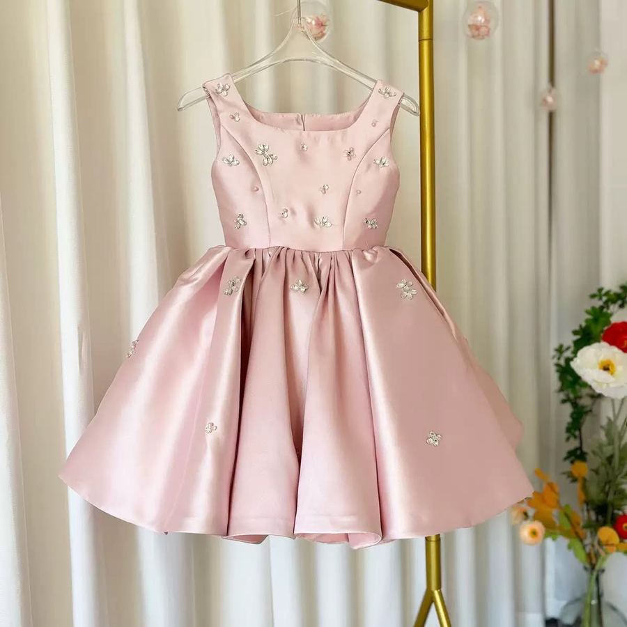 A blush satin flower-girl dress on a hanger.