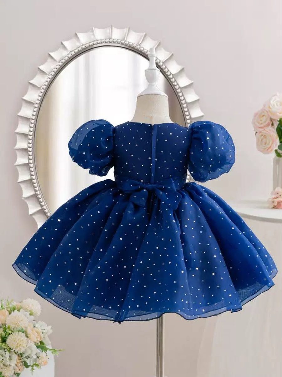 A navy dress with white dots, seen from the back, on a stand.